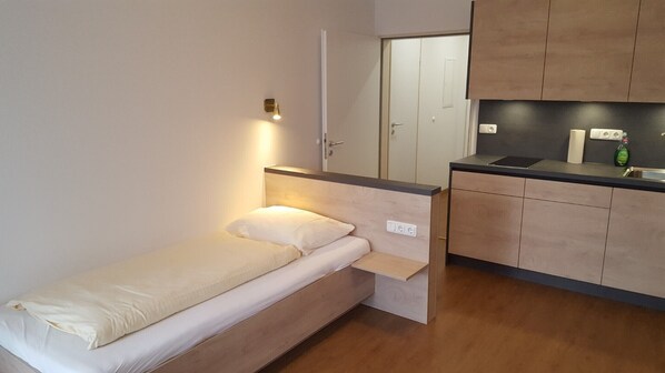 Una stanza compatta con un letto, un angolo cottura e un bagno collegato.