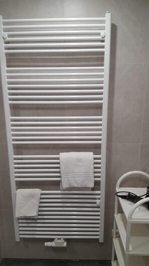 Un bagno con un portasciugamani bianco che contiene due asciugamani, un riscaldatore portatile bianco e un lavandino bianco con un cavo di alimentazione nero.