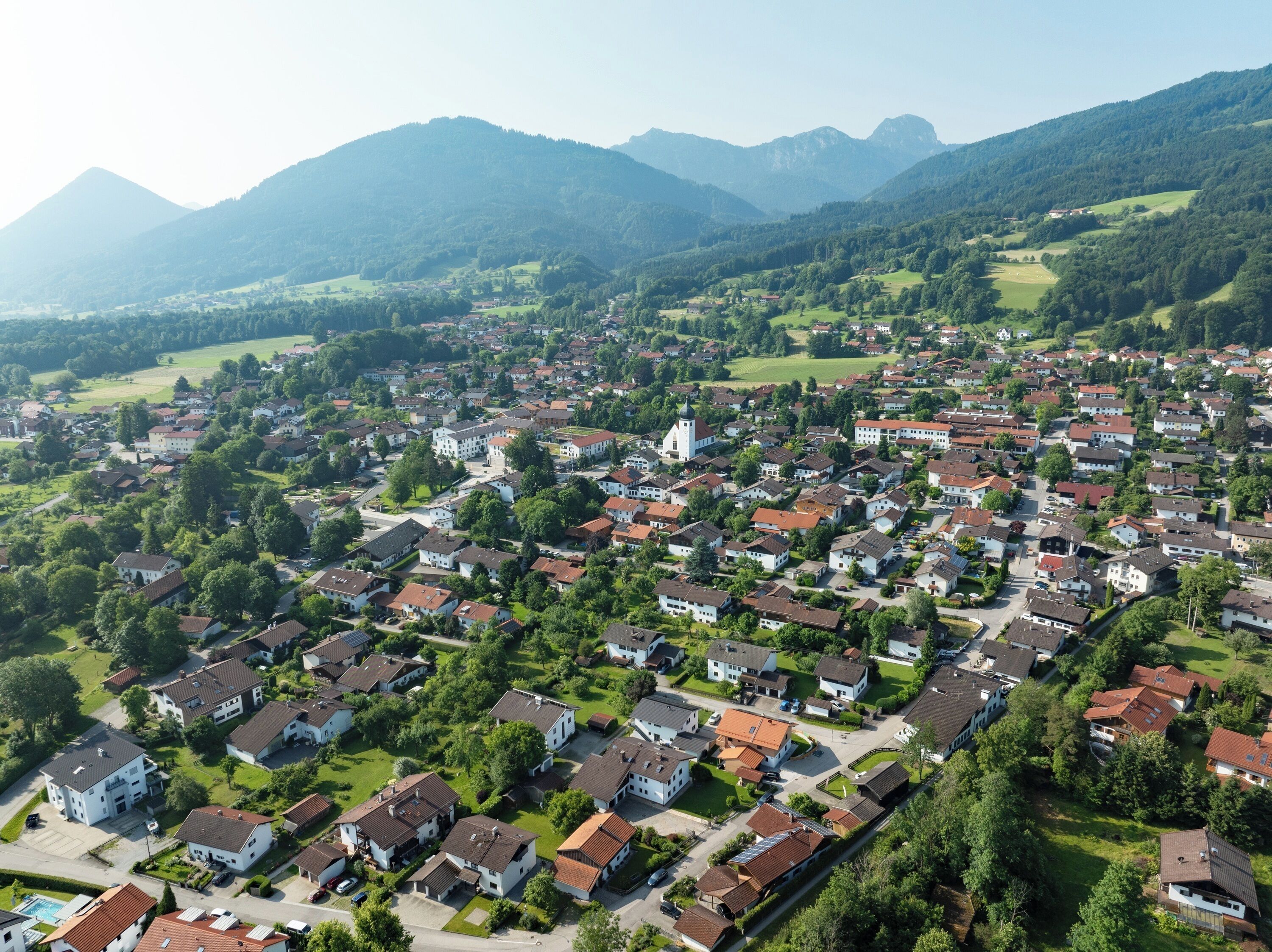 An aerial view of a residential area with houses, green spaces, and mountains in the background.
