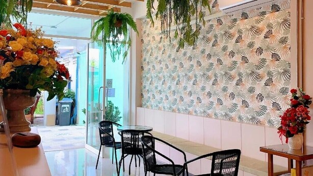 Um interior moderno com teto de madeira, plantas penduradas, parede estampada e área de estar com cadeiras pretas.