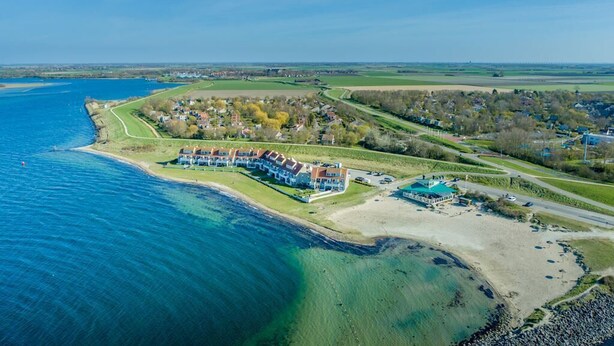 Une vue aérienne d’un hôtel situé sur la côte, avec une plage, un grand bâtiment doté de nombreux balcons et une pelouse bien entretenue.
