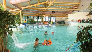 Une piscine intérieure à l’eau claire, entourée de plantes en pot et dotée d’un plafond haut avec des poutres apparentes.