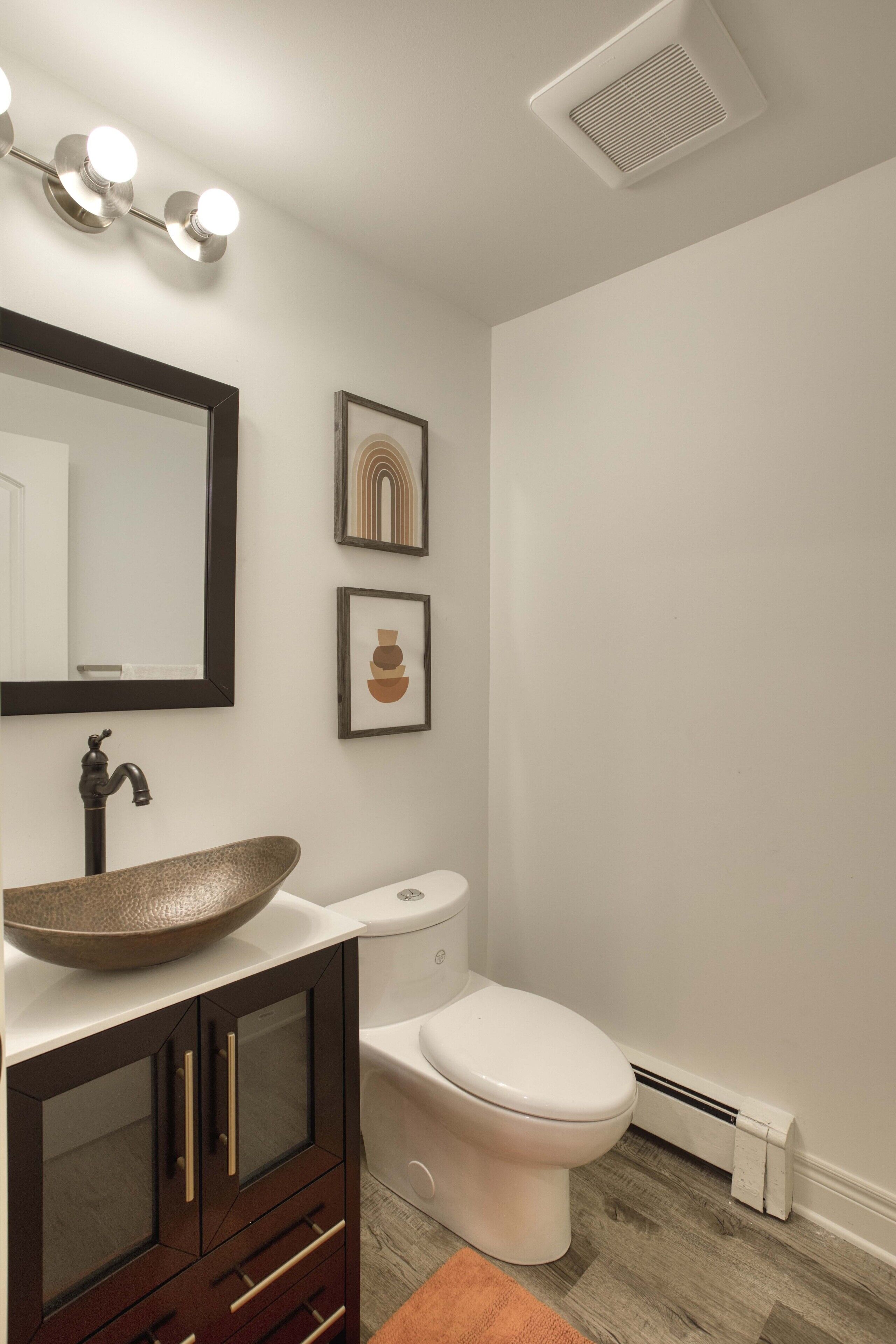 A modern bathroom with a vessel sink, dark wooden cabinet, white toilet, and a wall-mounted mirror.