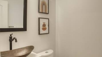 A modern bathroom with a vessel sink, dark wooden cabinet, white toilet, and a wall-mounted mirror.