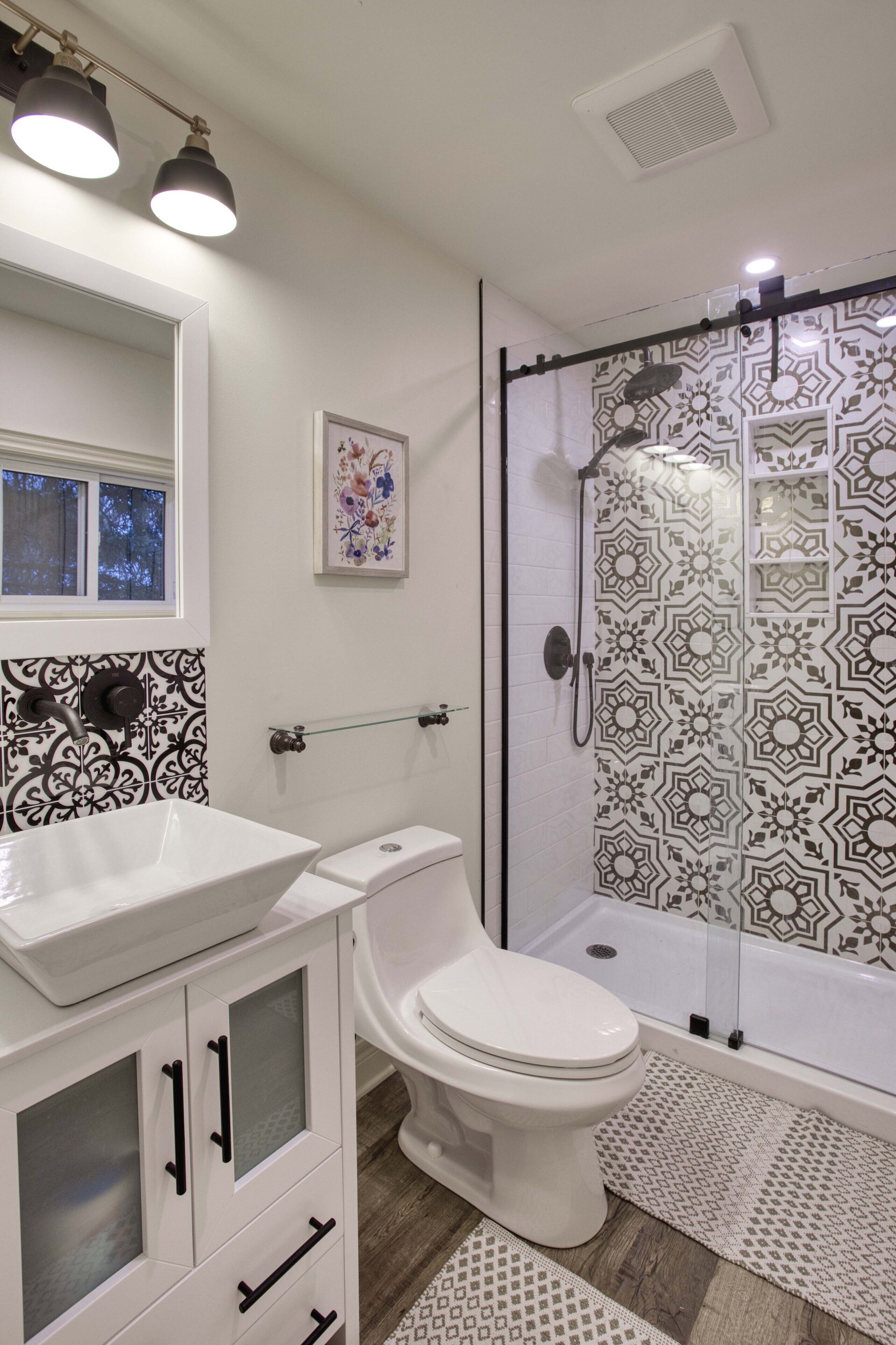 Casa de banho com lavatório branco, sanita e chuveiro com azulejos estampados.