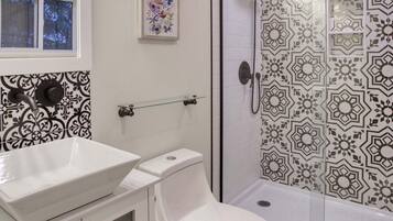 Casa de banho com lavatório branco, sanita e chuveiro com azulejos estampados.