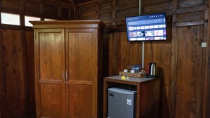 A wooden room with a large wardrobe, a small refrigerator, and a mounted TV displaying a streaming service interface. - Bali Desa Asri (Keroboken Kelod)