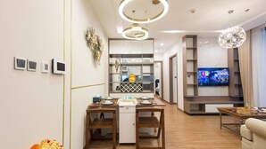 Una sala de estar moderna con piso de madera, un comedor con una mesa pequeña y sillas, una cocina con refrigerador y pileta, y un televisor montado en la pared.