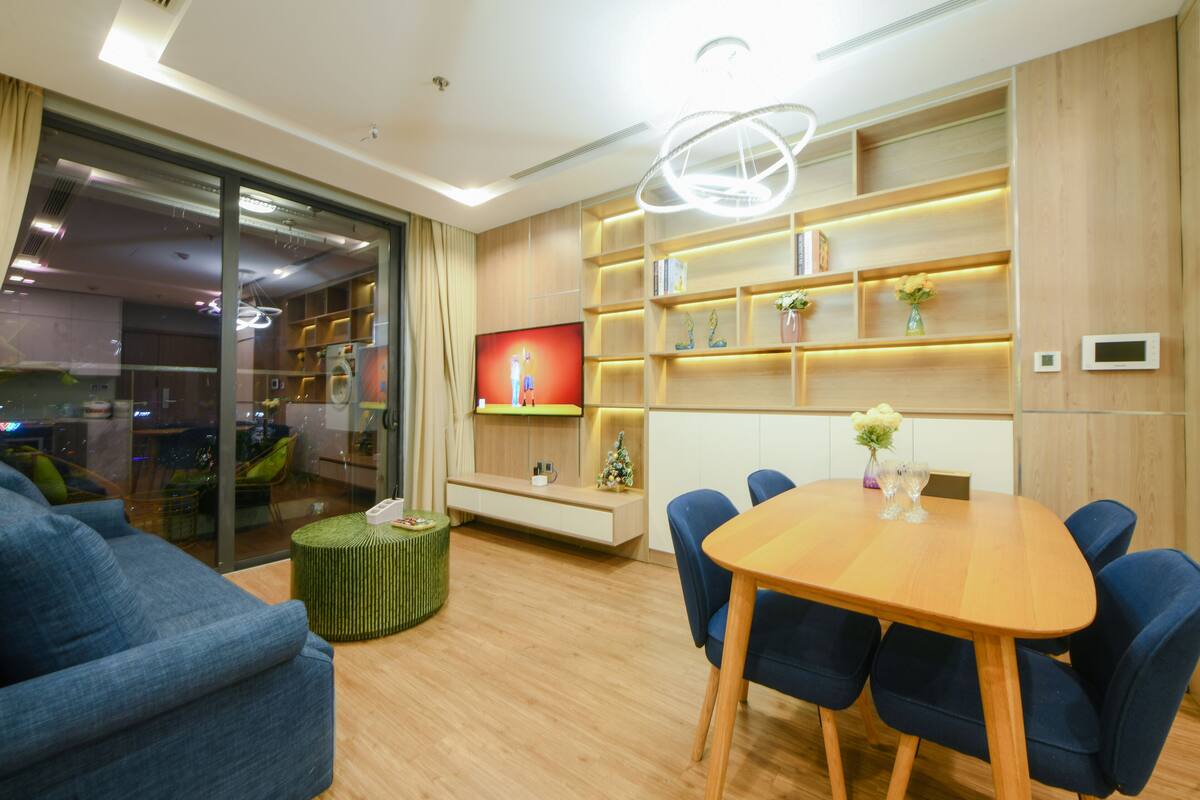 Un salon moderne avec une table à manger en bois, des chaises bleues, un téléviseur et une bibliothèque.