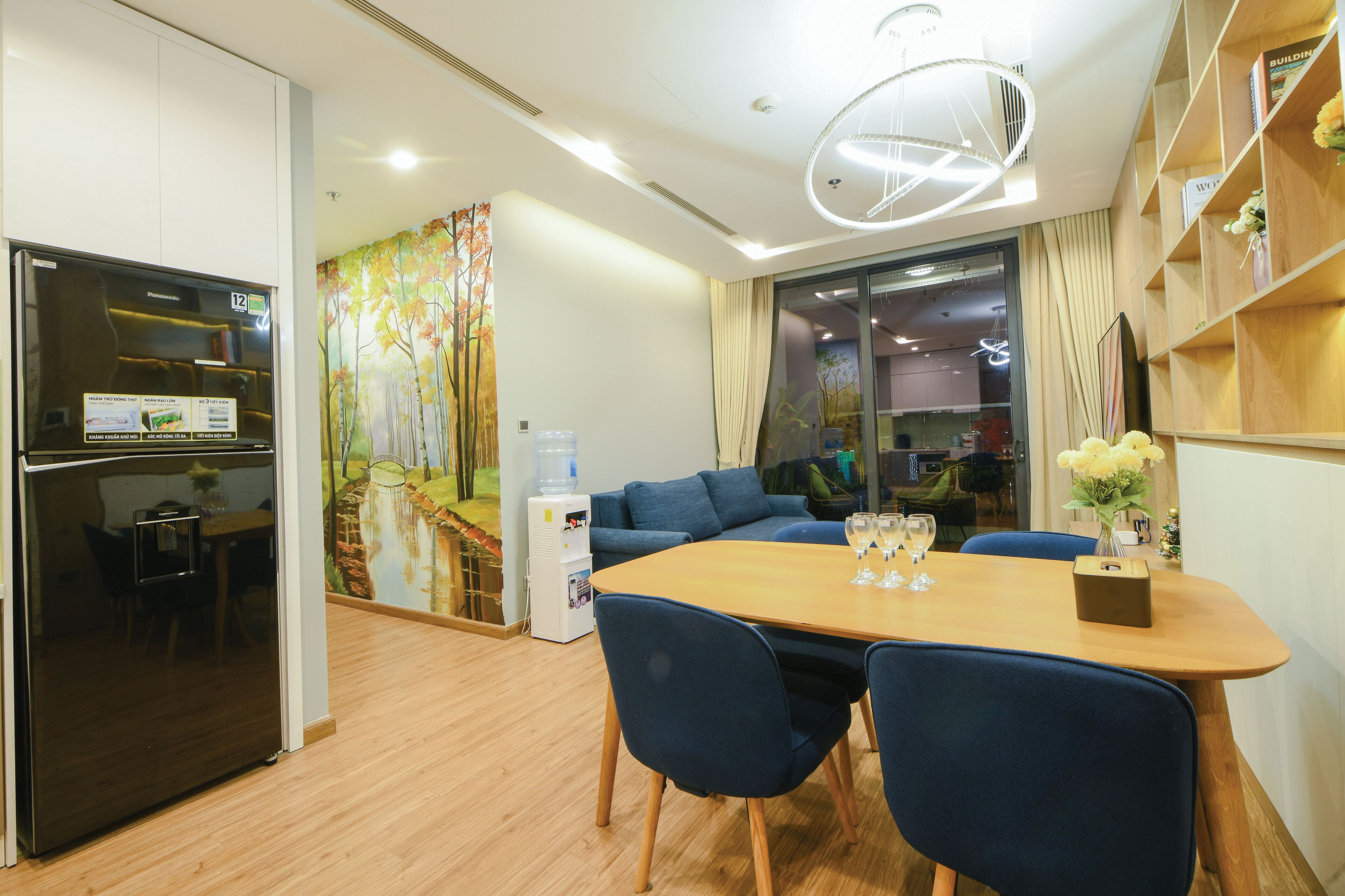 A modern kitchen with a refrigerator, a dining table with chairs, and a water dispenser.