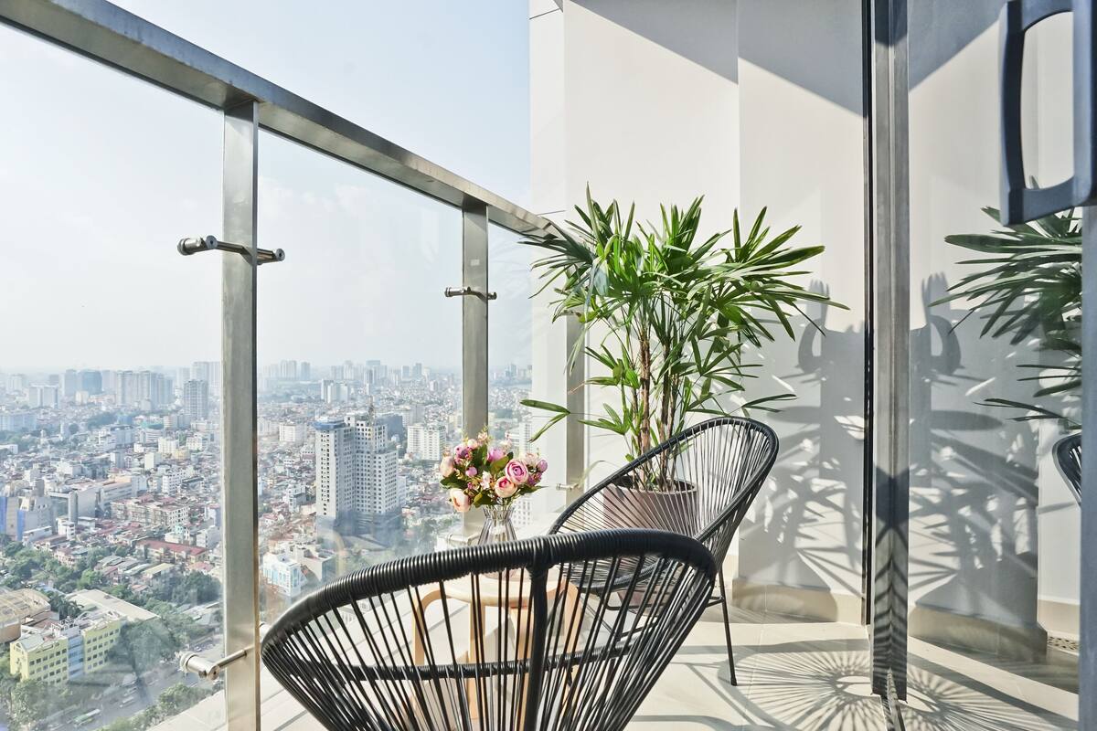 Un balcon avec vue sur la ville, une plante en pot et deux chaises.