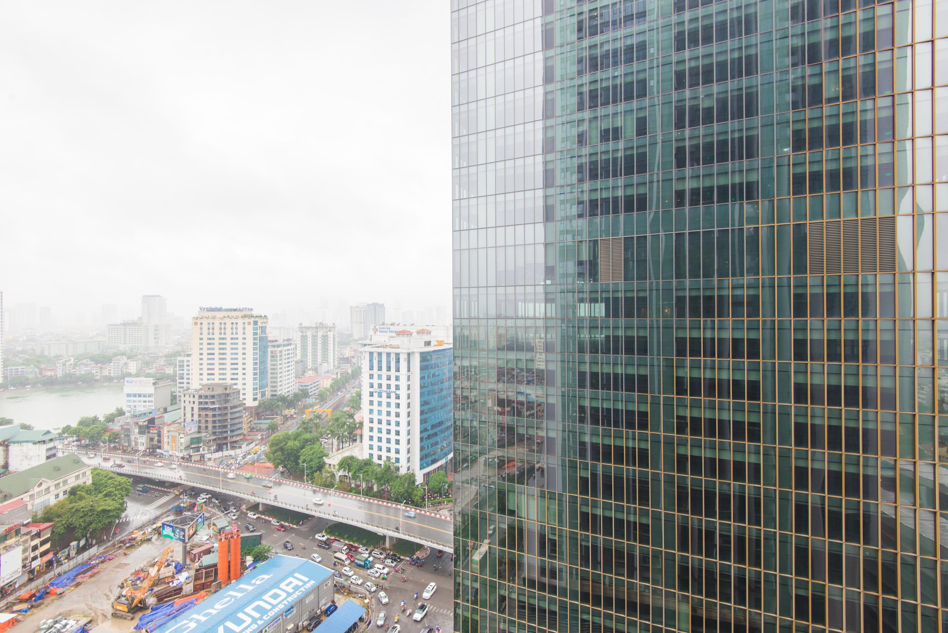 A high-rise building with a glass facade overlooking a busy urban area with a river and construction site.