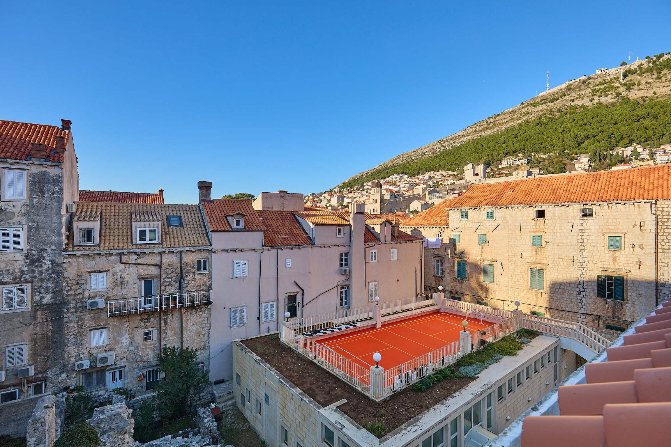 A courtyard with a tennis court surrounded by historic buildings with red-tiled roofs.