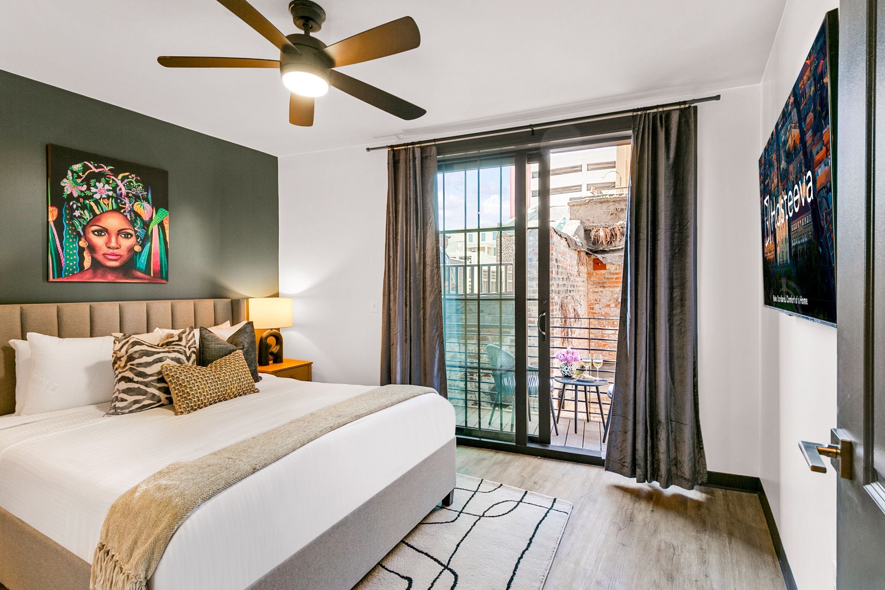 Habitación de hotel con una cama grande, un ventilador de techo, un cuadro en la pared, un balcón con vistas y un cartel en la pared.