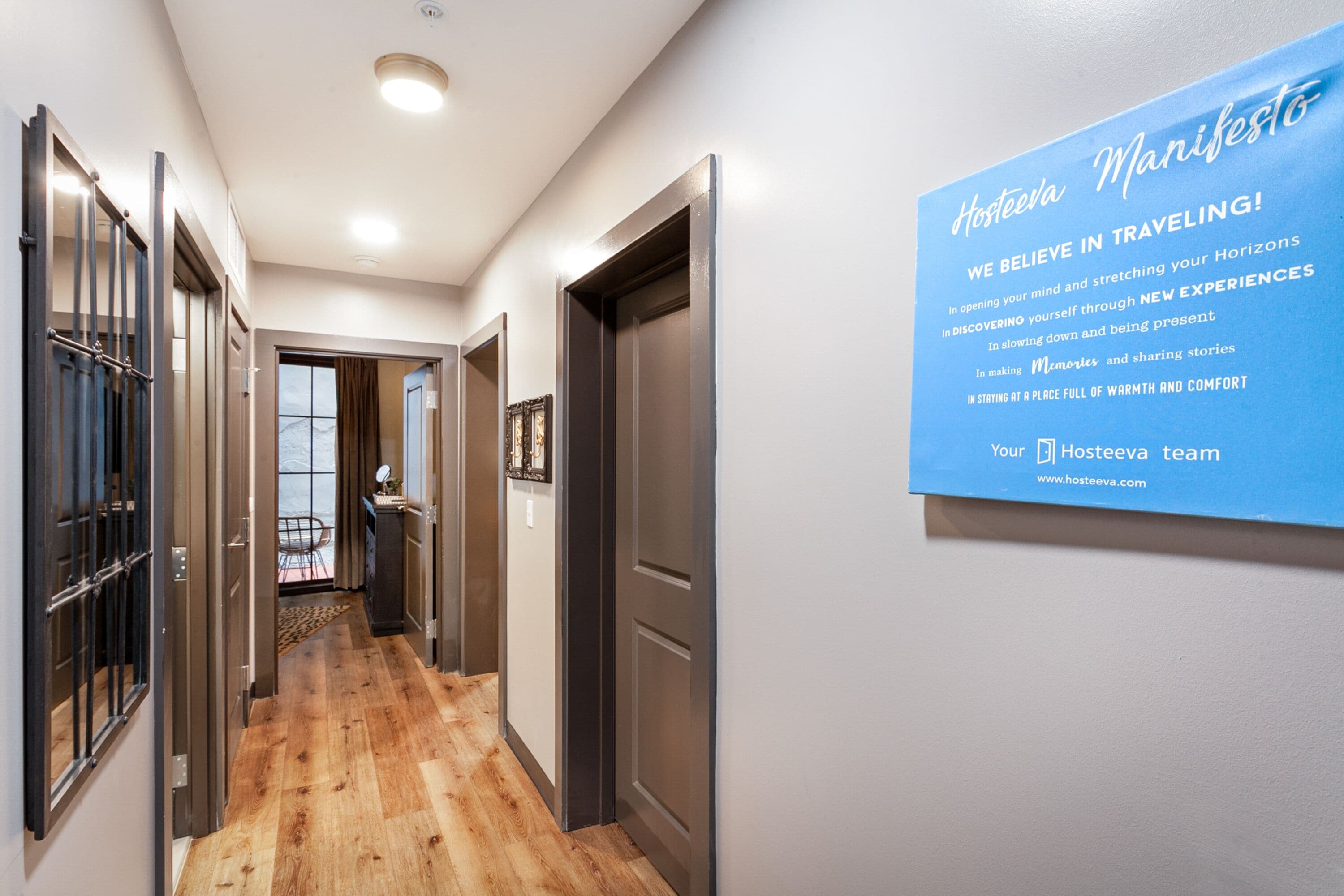 A hallway with wooden flooring, metal-framed doors, and a blue sign on the wall.
