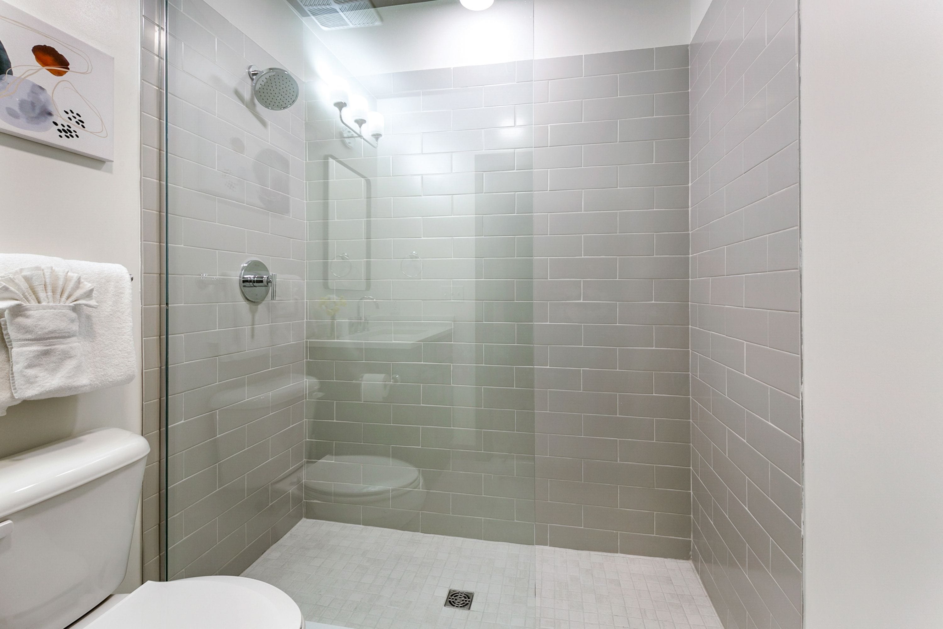 Une salle de bain moderne avec une douche à parois de verre, des murs recouverts de carreaux blancs, des toilettes et un lavabo.