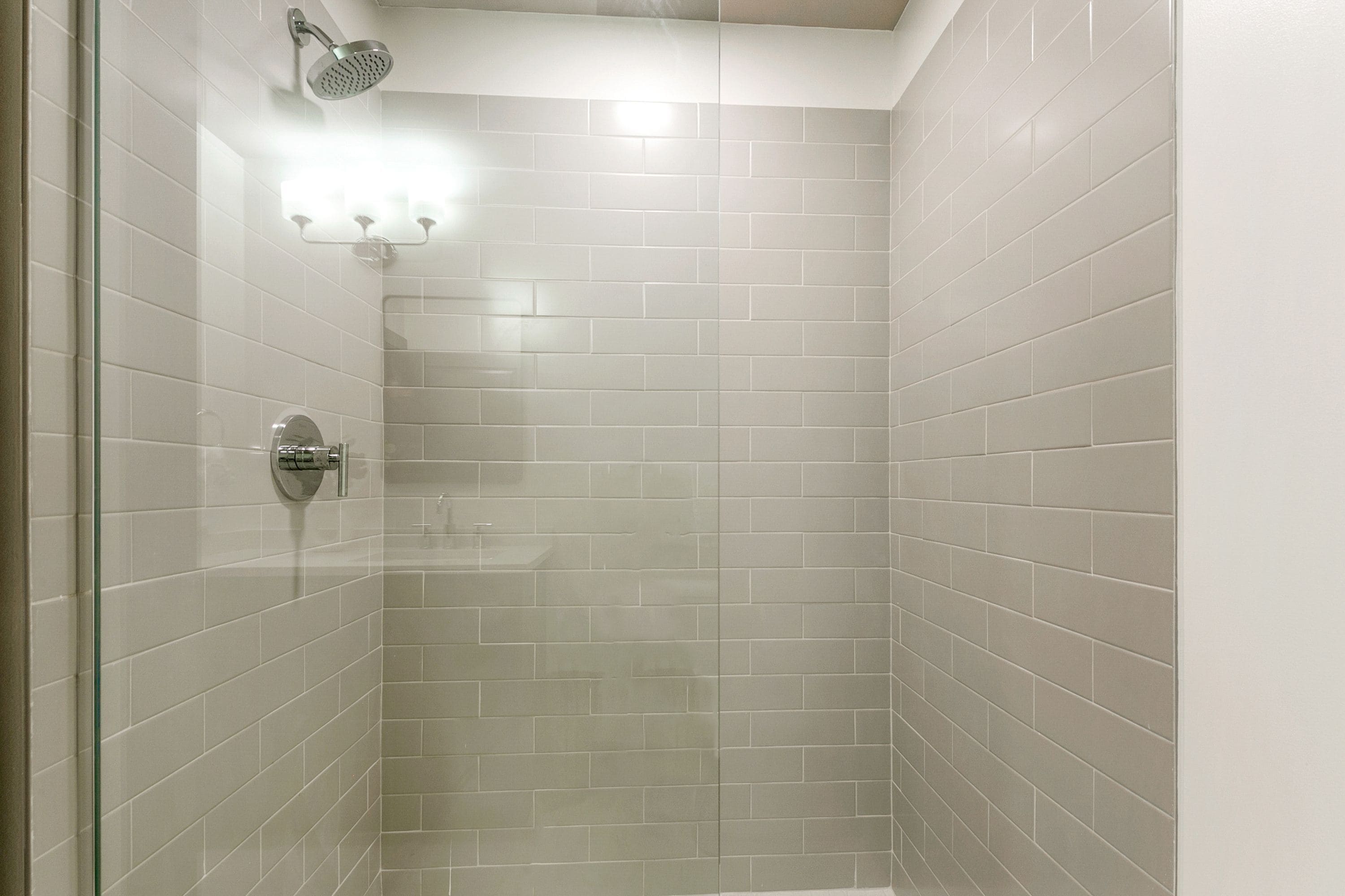 A shower with a glass door, a showerhead, and a wall-mounted light fixture.