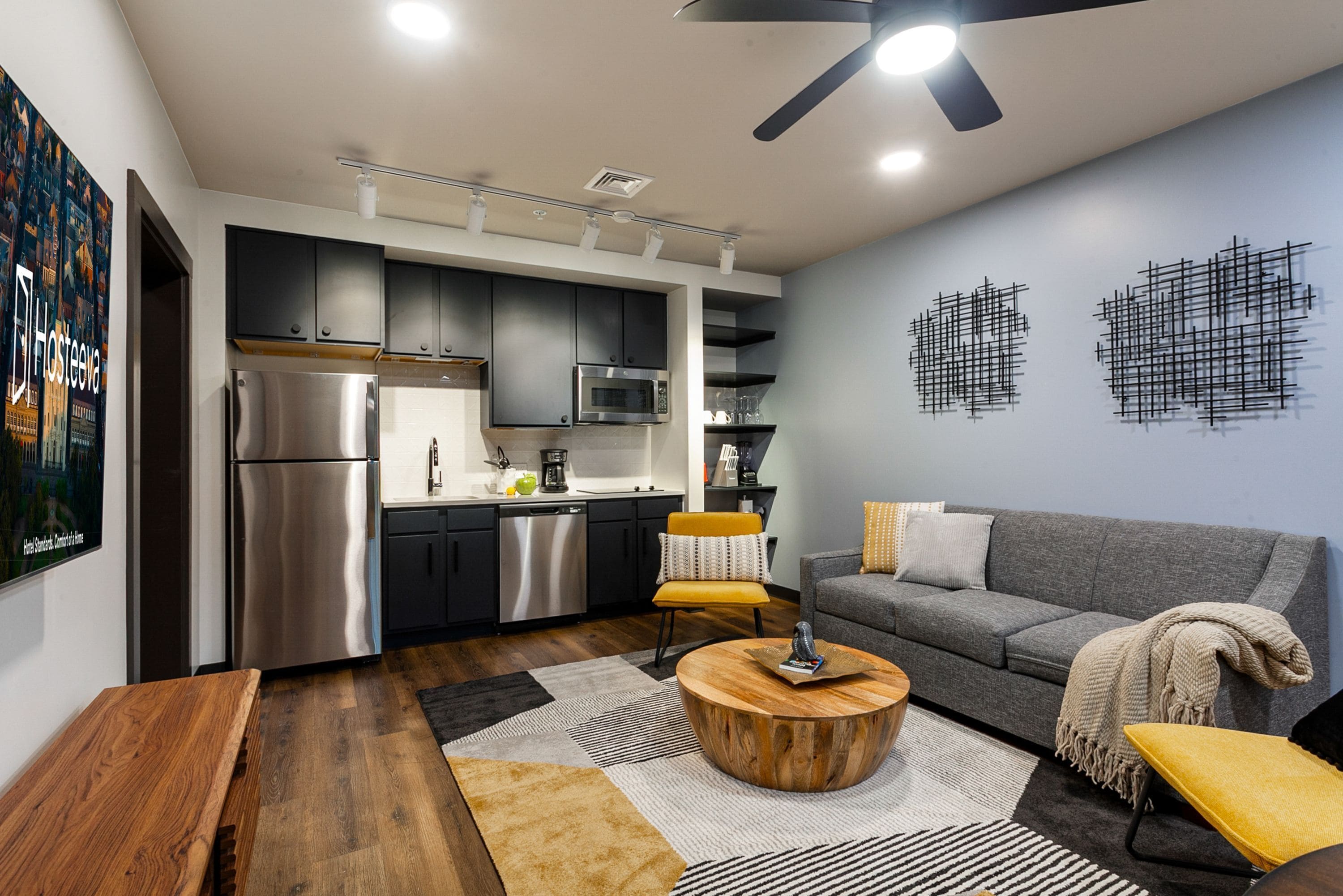 A modern kitchen with stainless steel appliances, a dining area with a round wooden table, and a grey sofa.