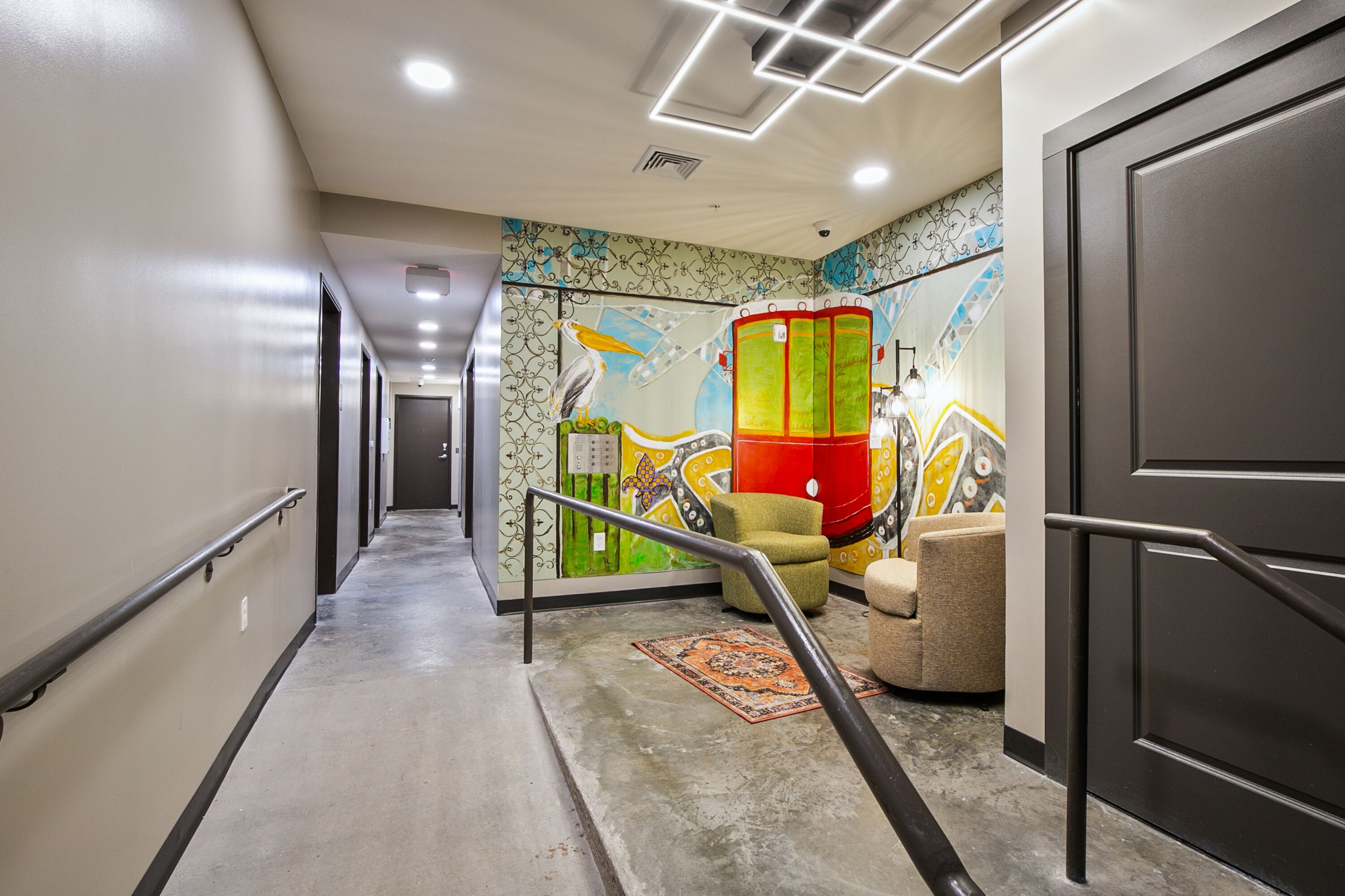 A hotel corridor with a handrail, a colorful mural, a staircase, and a door.