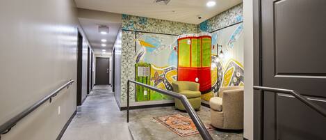A hotel corridor with a handrail, a colorful mural, a staircase, and a door.