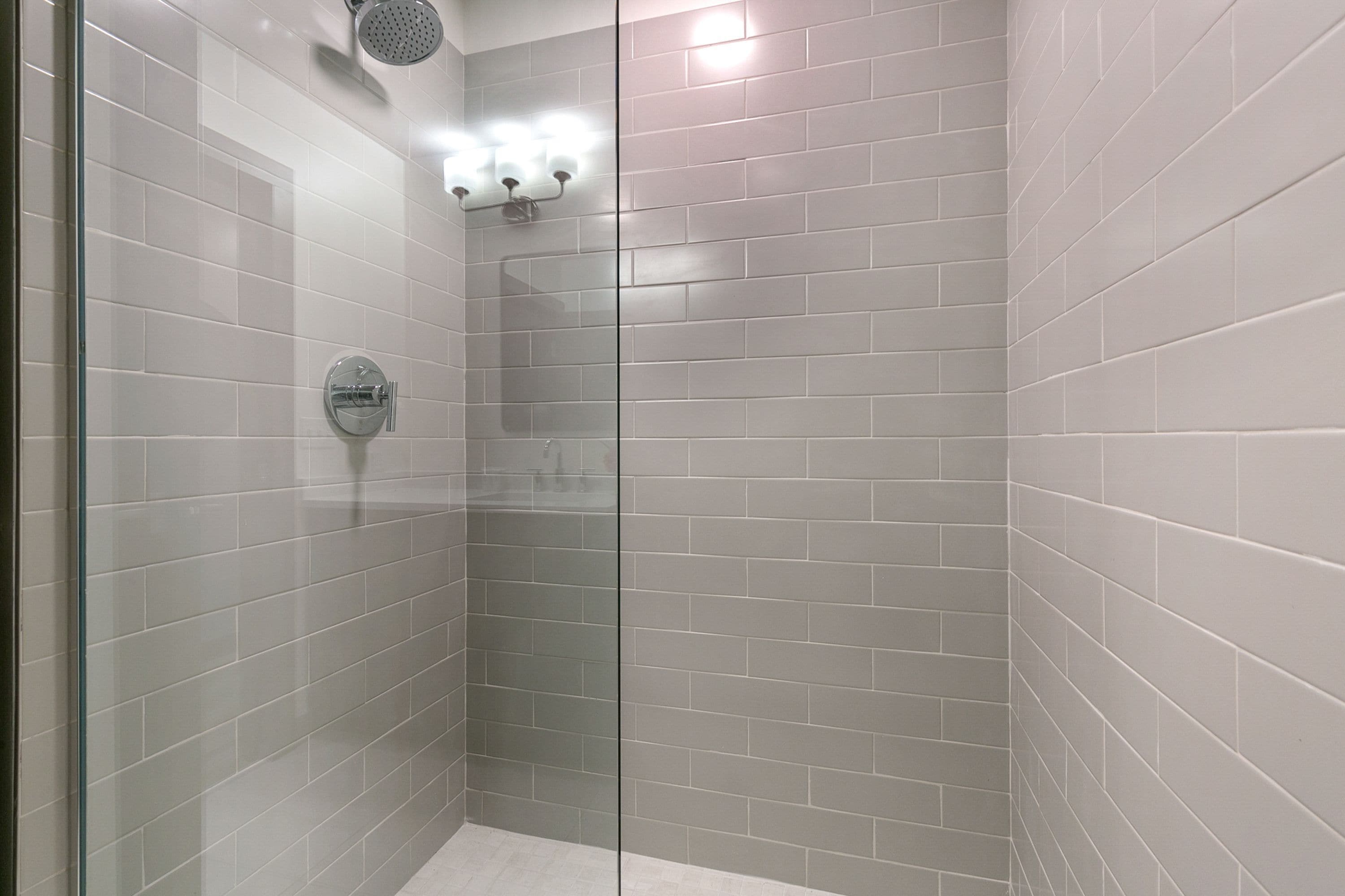 Une douche moderne avec une porte en verre, des murs carrelés et un pommeau de douche.
