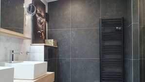 Een moderne badkamer met een grote spiegel, twee wastafels, een zwart toilet en een verwarmde handdoekrek.