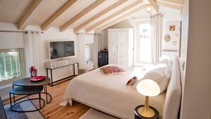 A bedroom with a large bed, a TV, a desk, and a window.
