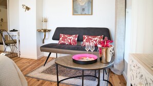 A modern living room with a grey sofa, red and white patterned pillows, a small round coffee table with a pink tray and glasses, and a decorative wall piece above the sofa.