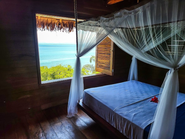 Una stanza con un letto, una finestra vista mare e una zanzariera.