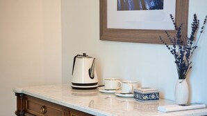 Une commode en bois avec des tiroirs, une bouilloire blanche et un vase de lavande posé sur un comptoir en marbre.
