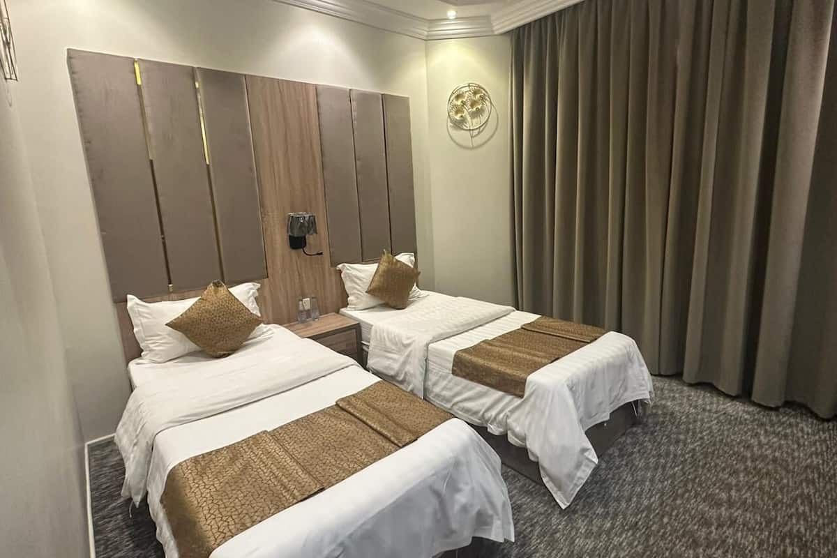 Ein Hotelzimmer mit zwei Betten, einem Kopfteil, einer Wanduhr und einem Vorhang.