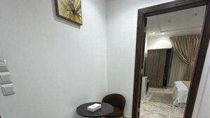 Habitación de hotel con suelo de mármol, una pequeña mesa redonda con dos sillas, un cuadro en la pared y vistas a la habitación contigua.