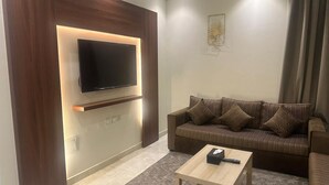 Una sala moderna con un televisor de pantalla plana montado en un panel de madera, un sofá marrón a rayas con varios cojines y una pequeña mesa de centro de madera.