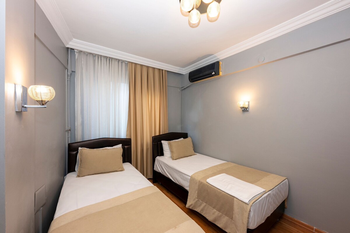 Une chambre d’hôtel avec deux lits simples, un ventilateur de plafond, un appareil de climatisation et des lampes fixées au mur.