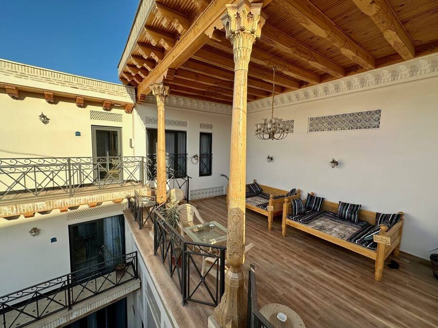 A spacious balcony with wooden flooring, a wooden ceiling, and a seating area with a sofa and chairs.
