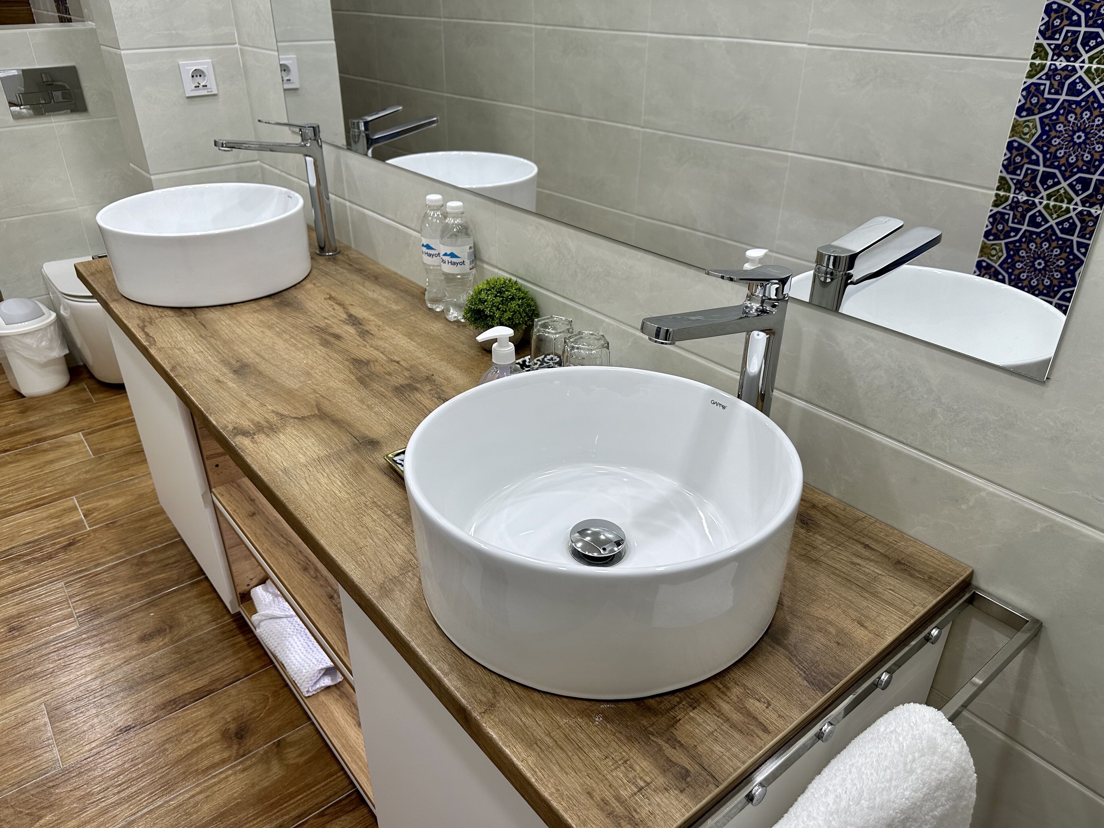 A modern bathroom with two sinks, a large mirror, and a wooden vanity.