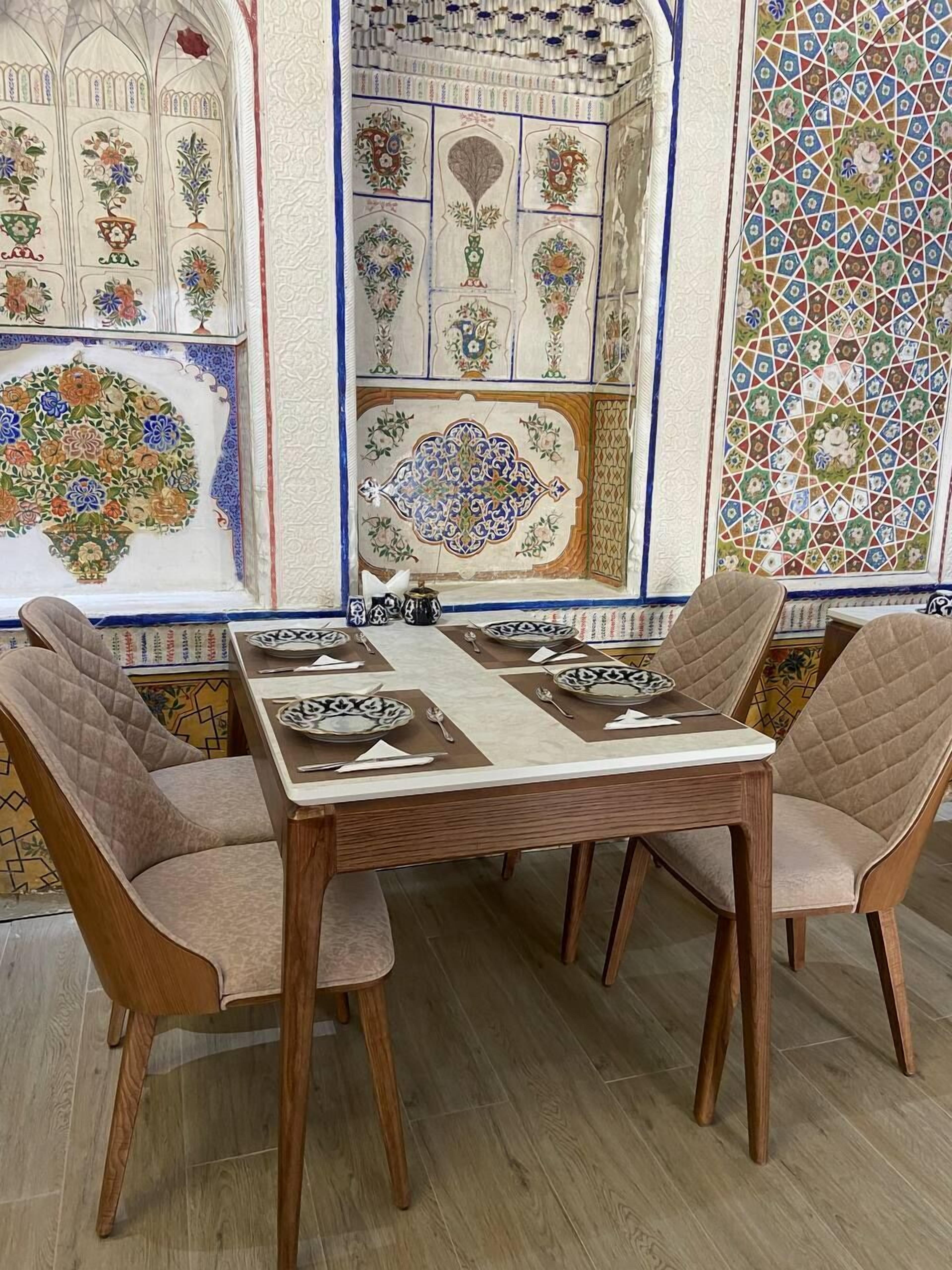 A dining area with a wooden table and cushioned chairs, surrounded by intricately designed tile walls.