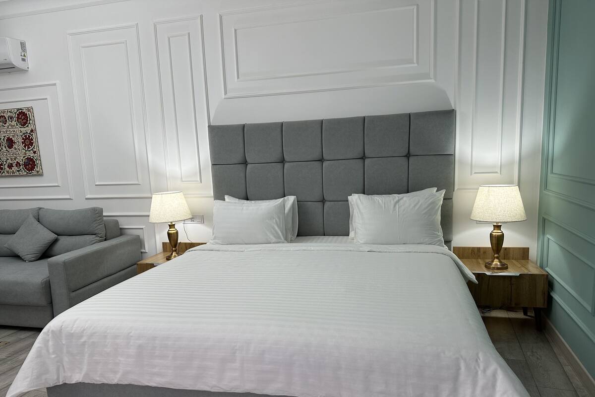 Une chambre à coucher bien aménagée, avec un grand lit, deux tables de chevet avec des lampes, un canapé gris et un élément décoratif mural.