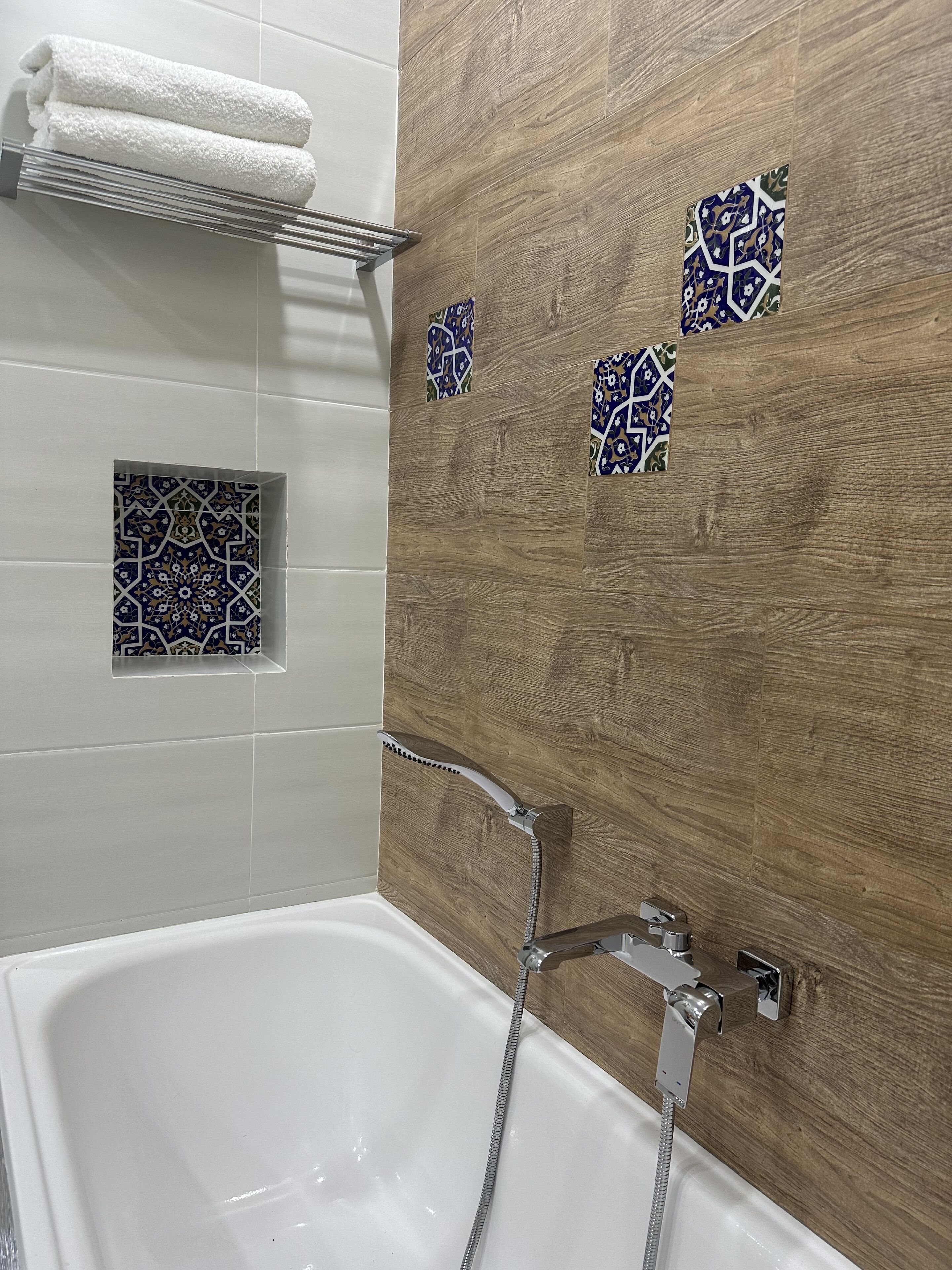 A modern bathroom with a white bathtub, wooden wall panels, and decorative tiles.