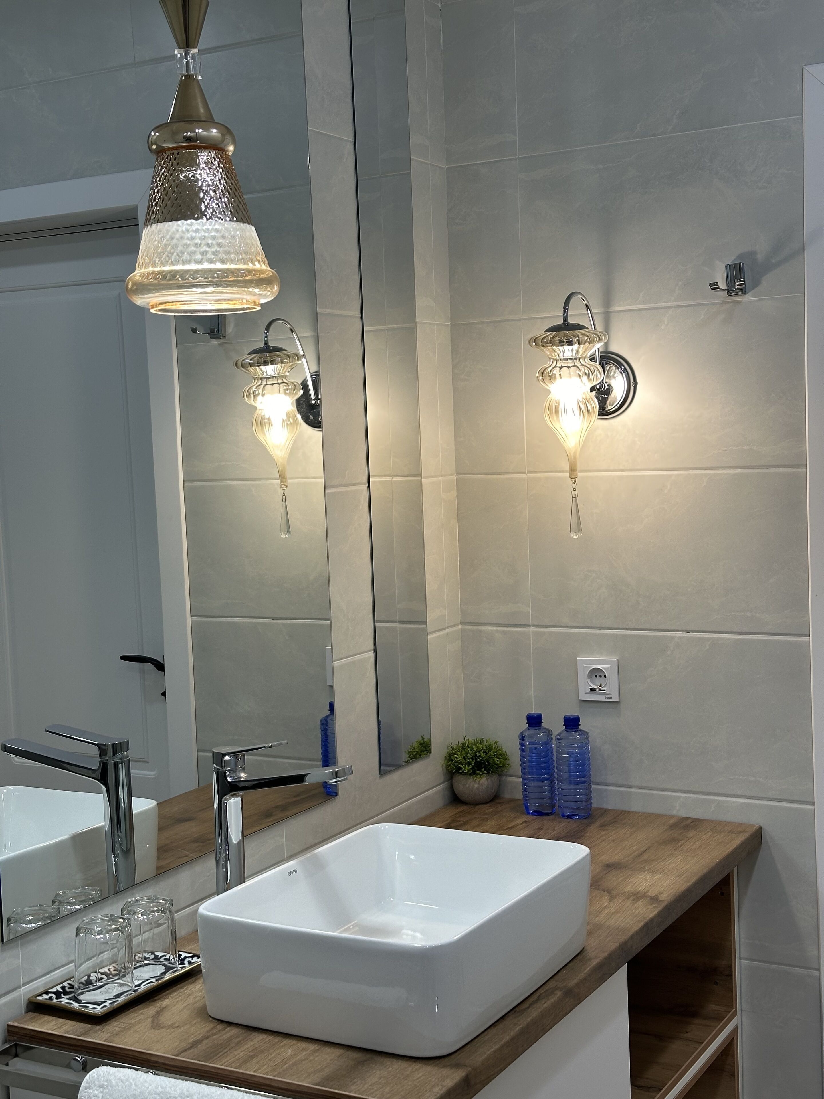 A modern bathroom with a white sink, two wall-mounted lights, and a mirror.