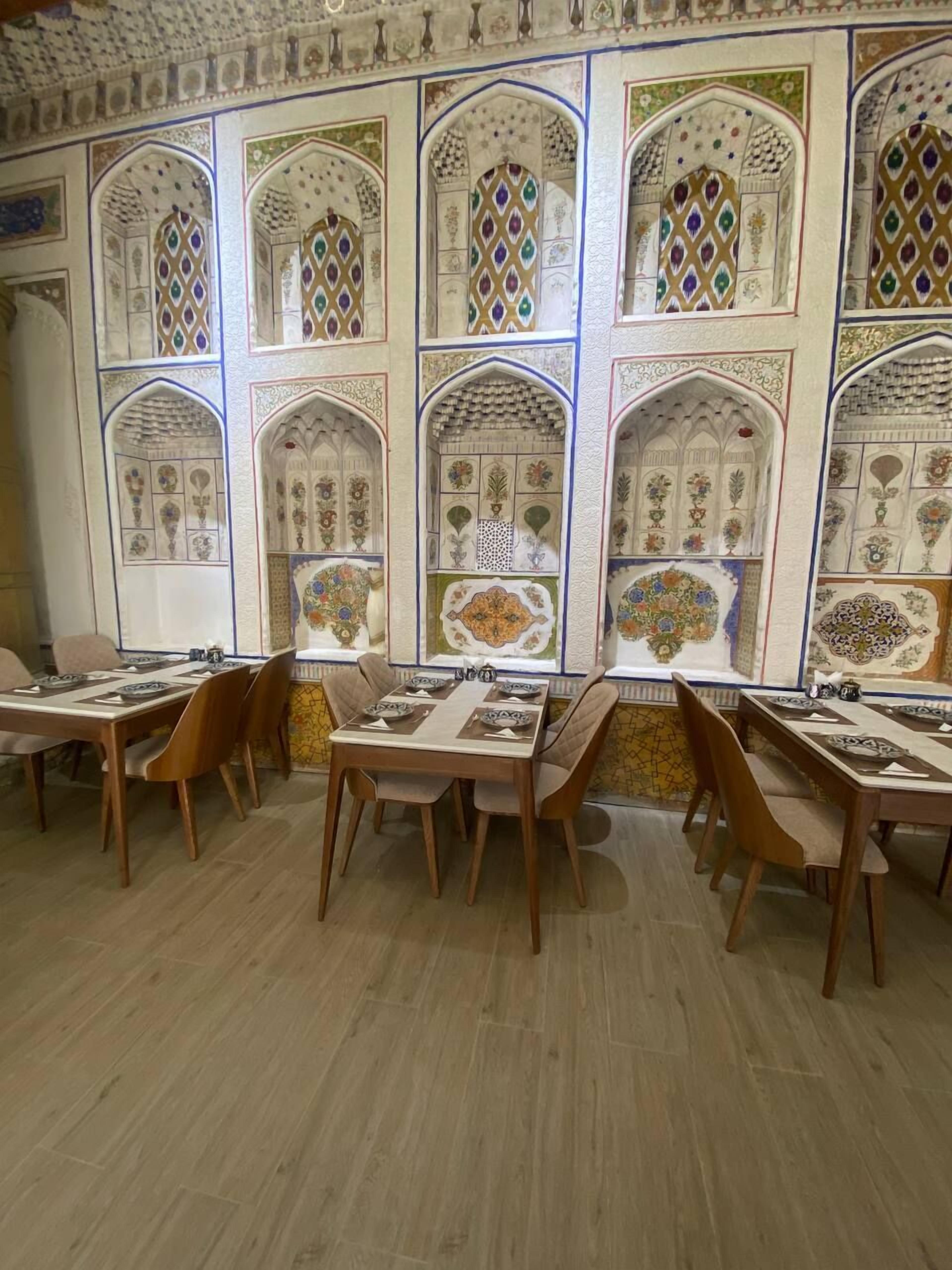 Un comedor con mesas y sillas de madera, decorado con detalles de azulejos intrincados y arcos.
