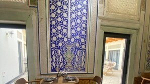 Uma sala de jantar com mesa posta para quatro pessoas, rodeada por cadeiras, e uma parede decorativa com padrões elaborados.