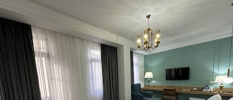 A hotel room with a large bed, a desk with a lamp, a television, and a minibar.