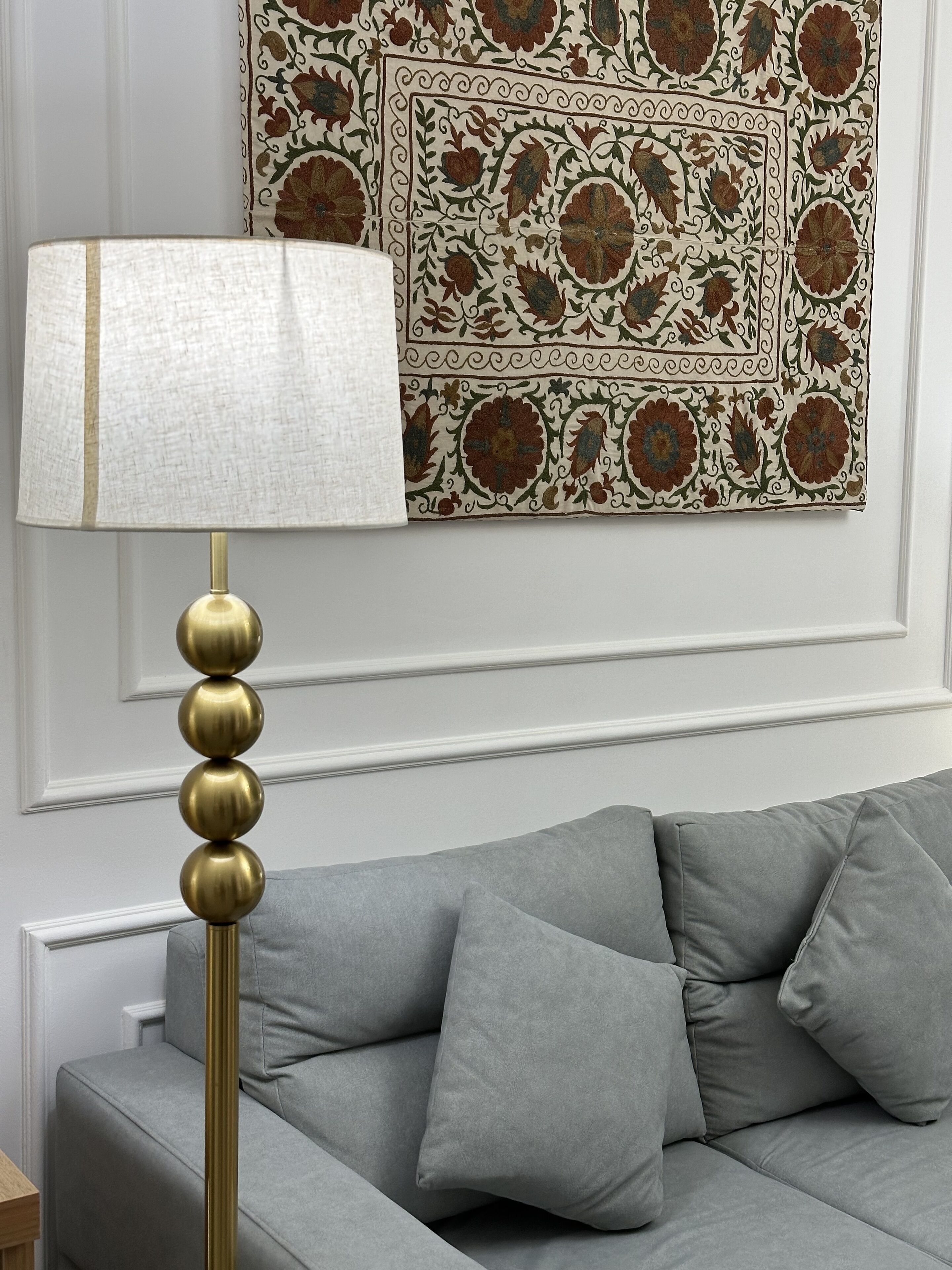 A modern living room with a grey sofa, a gold floor lamp, and a decorative wall hanging.