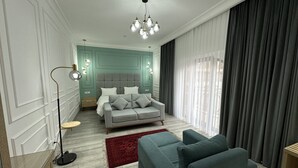 Quarto moderno com um sofá cinzento, um tapete vermelho, uma cama com roupa de cama cinza e um candelabro.