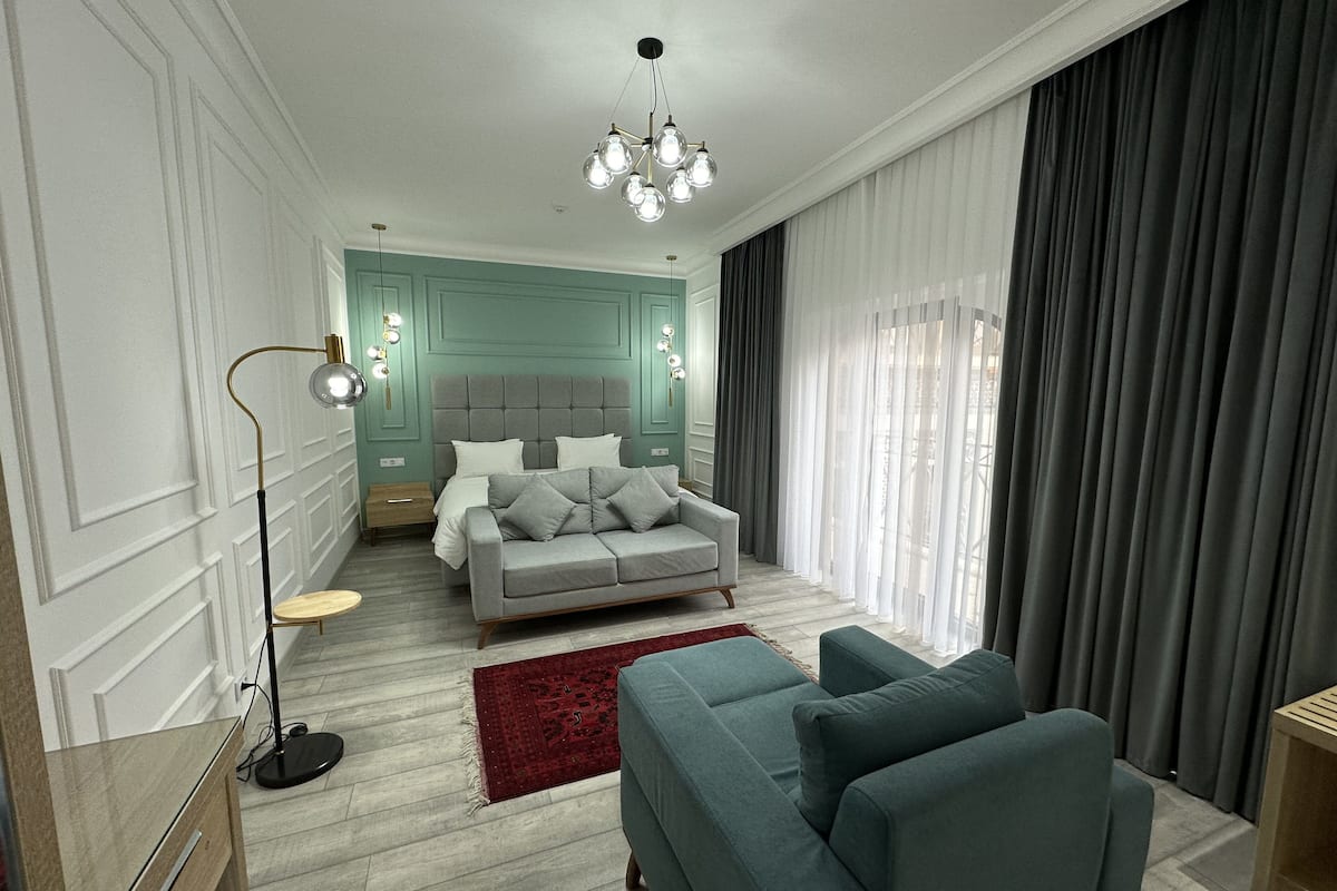 Une chambre à coucher moderne avec un canapé gris, un tapis rouge, un lit avec une literie grise et un lustre.