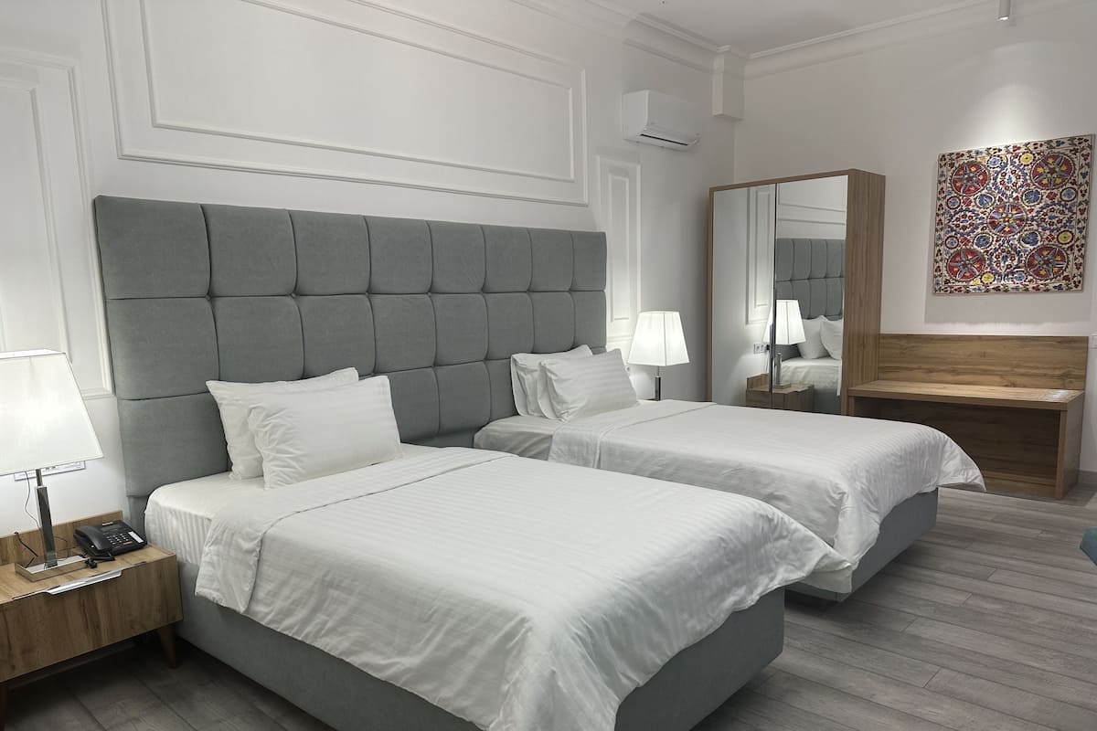 Une chambre d’hôtel avec deux lits, une table de chevet avec une lampe, un miroir et un élément décoratif mural.