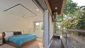 A bedroom with a bed, bedside table, and a balcony with a view of trees.