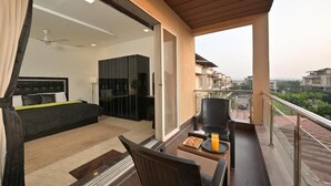 A balcony with a bed, a chair, and a table with a drink.