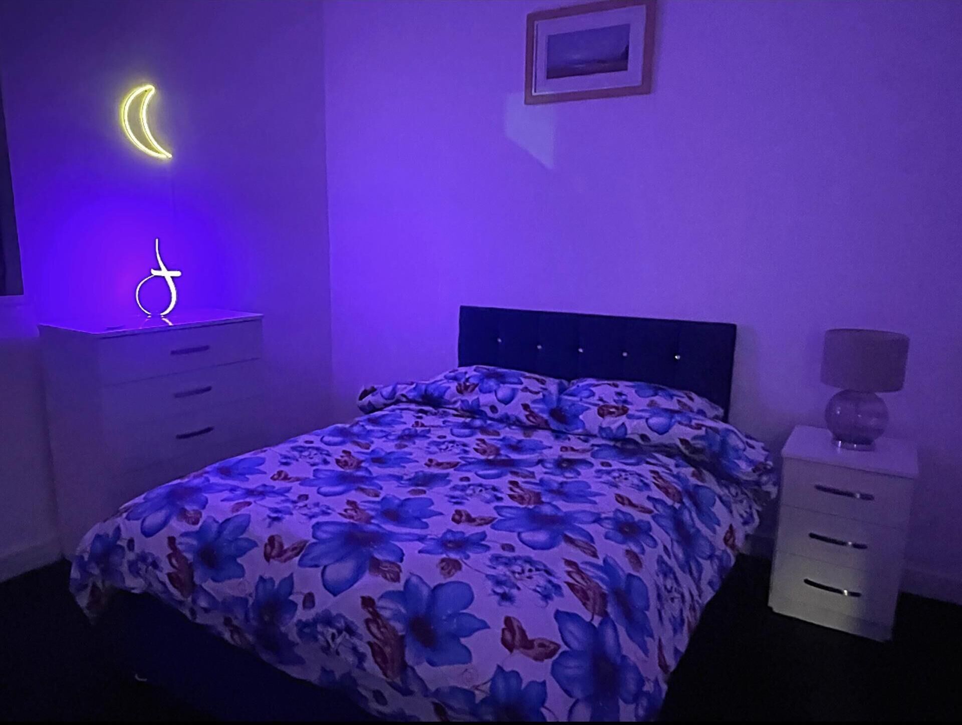 A bedroom with a bed, a nightstand, a lamp, and a wall-mounted light.